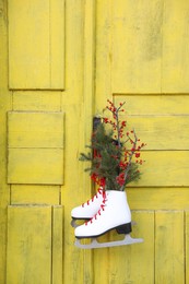 Pair of ice skates with Christmas decor hanging on old yellow door
