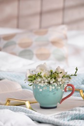Beautiful bright flowers in cup, open book and tray on bed