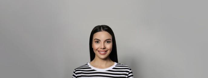 Portrait of happy young woman with beautiful black hair and charming smile on light grey background. Horizontal banner design