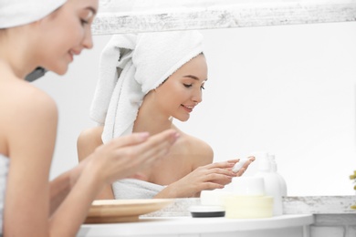 Teenage girl with acne problem using cream while looking in mirror indoors