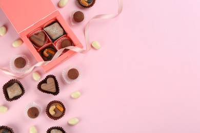 Photo of Different delicious chocolate candies with box on light pink background, flat lay. Space for text
