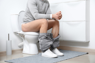 Man sitting on toilet bowl in bathroom, closeup