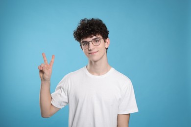 Photo of Portrait of cute teenage boy wearing glasses and showing peace gesture on light blue background