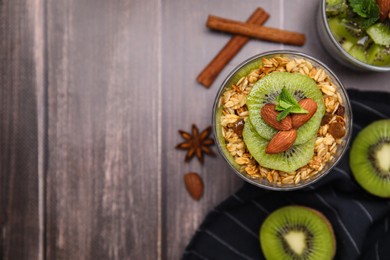 Photo of Delicious dessert with kiwi, muesli and almonds on wooden table, flat lay. Space for text