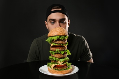 Young hungry man and huge burger on black background