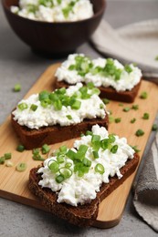 Photo of Bread with cottage cheese and green onion on light grey table, closeup