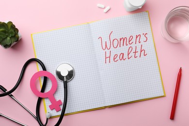 Photo of Flat lay composition of notebook with words Women Health and female gender sign on pink background