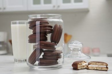 Jar with delicious choco pies and glass of milk on white table in kitchen