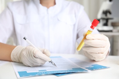 Doctor holding test tube with urine sample for analysis at table in laboratory, closeup