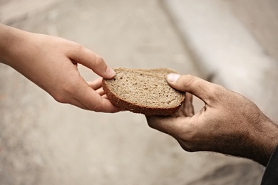 Woman giving poor homeless person pieces of bread outdoors, closeup