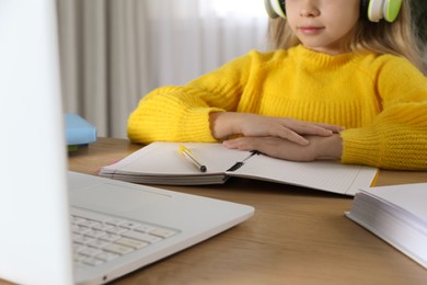 Photo of Cute little girl with modern laptop studying online at home, closeup. E-learning