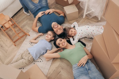 Happy family lying on floor near moving boxes in new house, top view