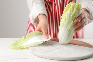 Woman separating leaf from fresh chinese cabbage at white marble table, closeup
