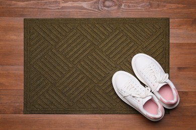 New clean door mat with shoes on wooden floor, flat lay