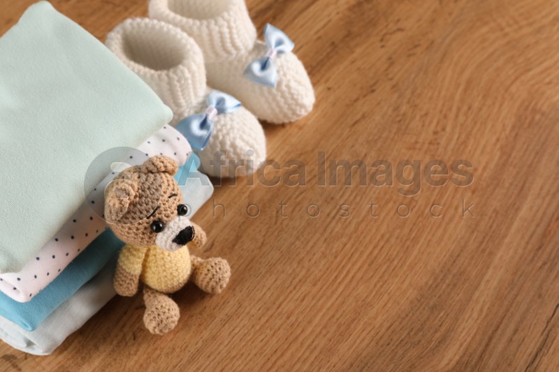 Stack of baby boy's clothes, booties and toy on wooden table, above view. Space for text