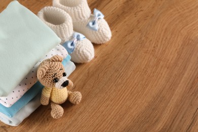 Stack of baby boy's clothes, booties and toy on wooden table, above view. Space for text
