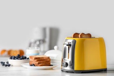 Yellow toaster with roasted bread slices, blueberries and glass of milk on white marble table