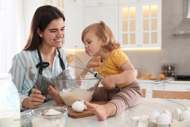 Photo of Mother and her little daughter cooking dough together in kitchen