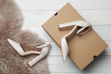 Pair of stylish shoes, cardboard box and faux fur on white wooden background, flat lay