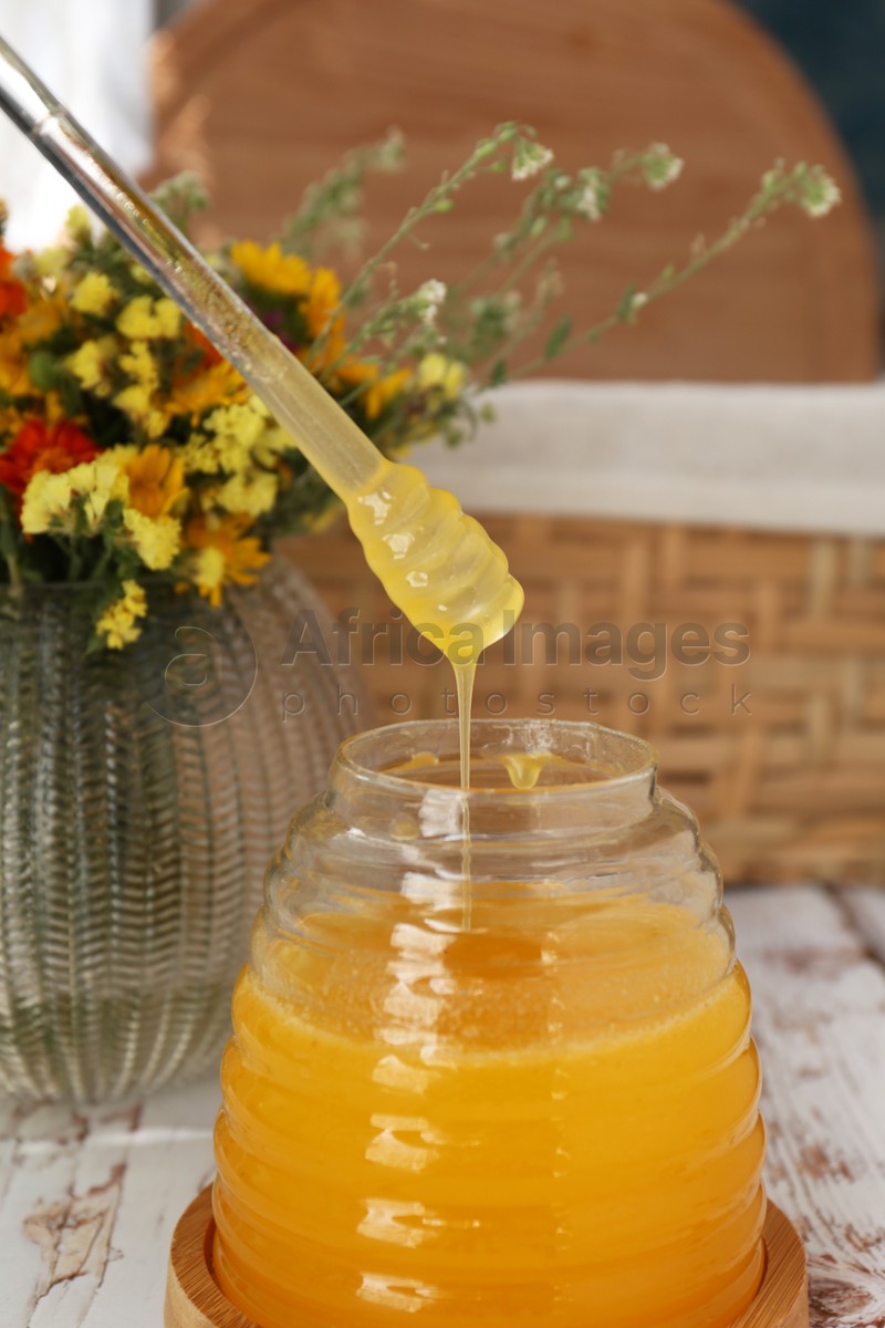 Delicious fresh honey and beautiful flowers on white wooden table indoors