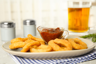 Delicious crunchy fried onion rings and sauce on grey marble table