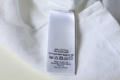 Clothing label with care symbols and material content on white shirt, closeup view