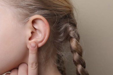 Cute little girl pointing at her ear on beige background, closeup