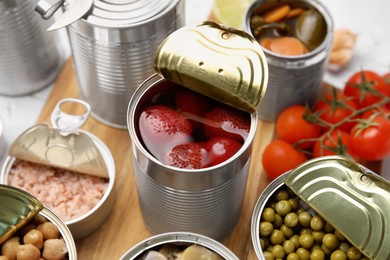 Photo of Open tin cans with different preserved products on wooden board, closeup