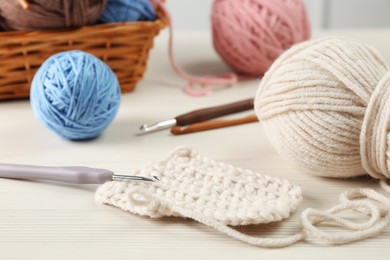Knitting, crochet hook and clews on white wooden table