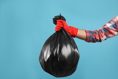 Man holding full garbage bag on light blue background, closeup