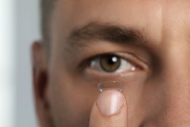 Man putting contact lens in his eye on blurred background, closeup