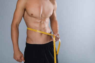 Shirtless man with slim body and measuring tape around his waist on grey background, closeup. Space for text