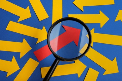 Photo of Recruitment process, searching for employee. View through magnifying glass of red paper arrow among yellow ones on blue background, flat lay