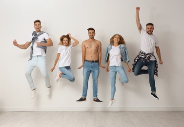 Group of young people in jeans jumping near light wall