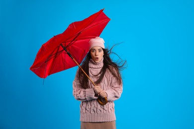 Emotional woman with broken umbrella caught in gust of wind on light blue background