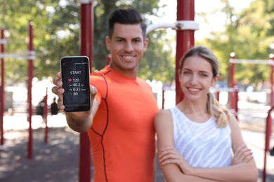 Couple showing smartphone with fitness app outdoors, focus on device