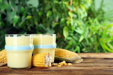Photo of Freshly made corn juice in glass on wooden table against blurred background. Space for text