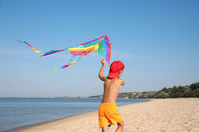 Cute little child with kite running at beach on sunny day