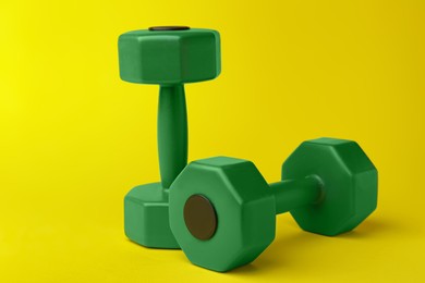 Two green dumbbells on yellow background, closeup