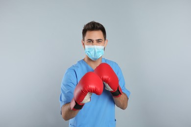 Doctor with protective mask and boxing gloves on light grey background. Strong immunity concept
