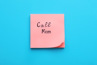 Photo of Paper note with phrase Call mom on blue background, top view