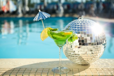 Shiny disco ball and refreshing cocktail on edge of swimming pool. Party items
