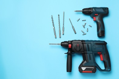 Modern electric power drill and different bits on light blue background, flat lay. Space for text