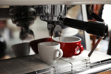 Aromatic coffee pouring into cups from modern machine, closeup