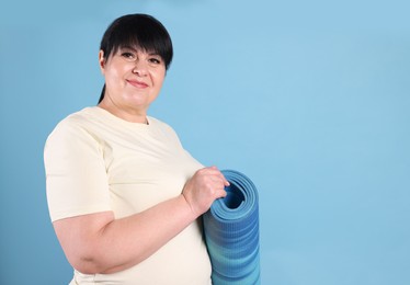 Photo of Happy overweight mature woman with yoga mat on light blue background, space for text