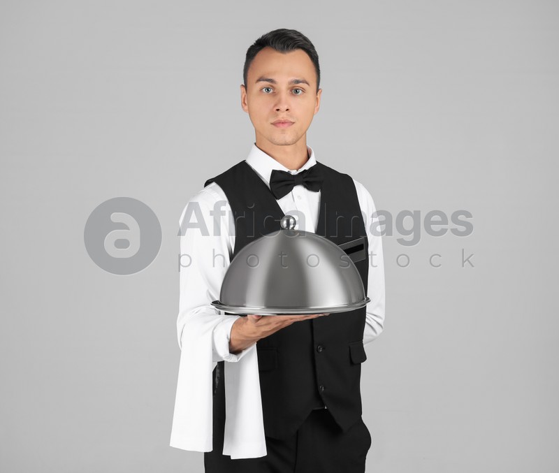 Waiter holding metal tray with lid on grey background