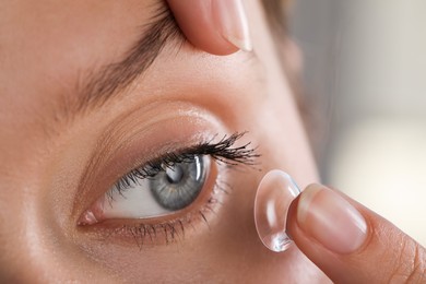 Young woman putting contact lens in her eye on blurred background, closeup