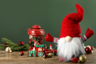 Cute Christmas gnome and festive decor on wooden table against green background. Space for text