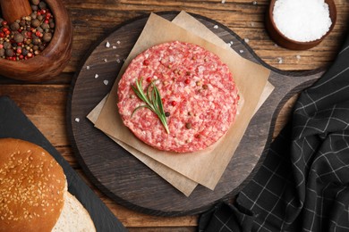 Raw hamburger patties with rosemary and spices on wooden table, flat lay