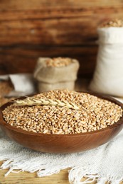 Photo of Bowl of wheat grains and spikelet on wooden table
